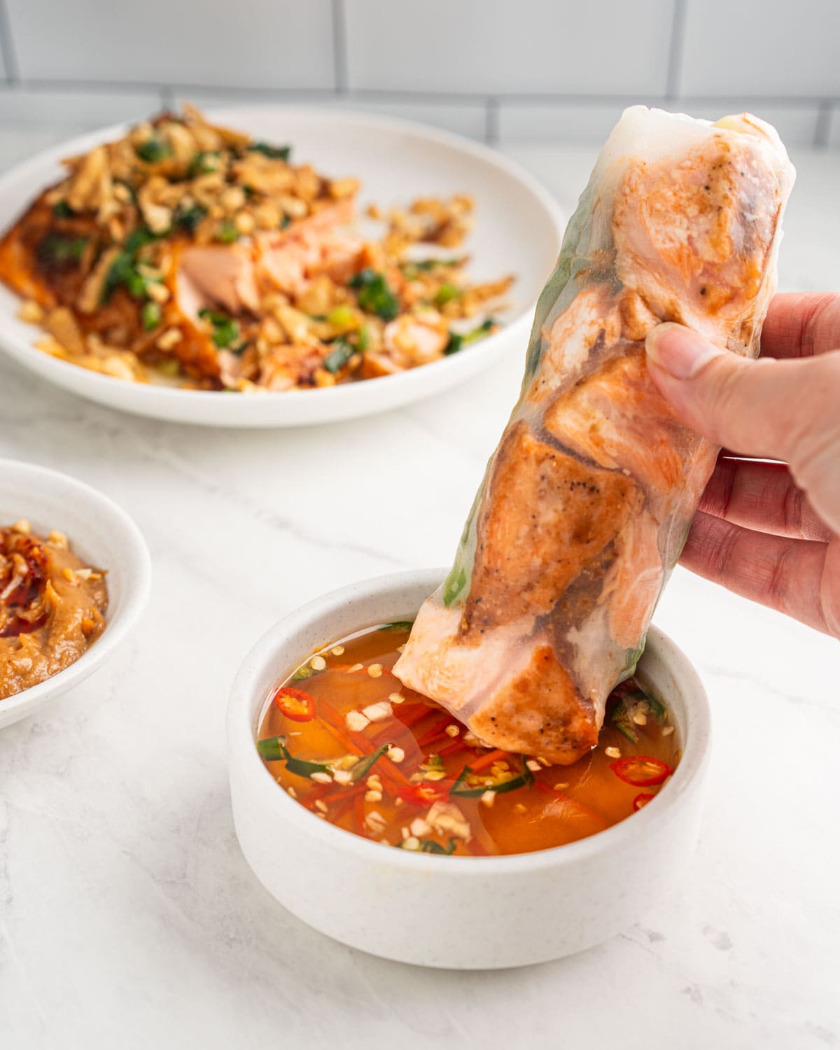 hand dipping salmon spring roll into fish sauce dip.