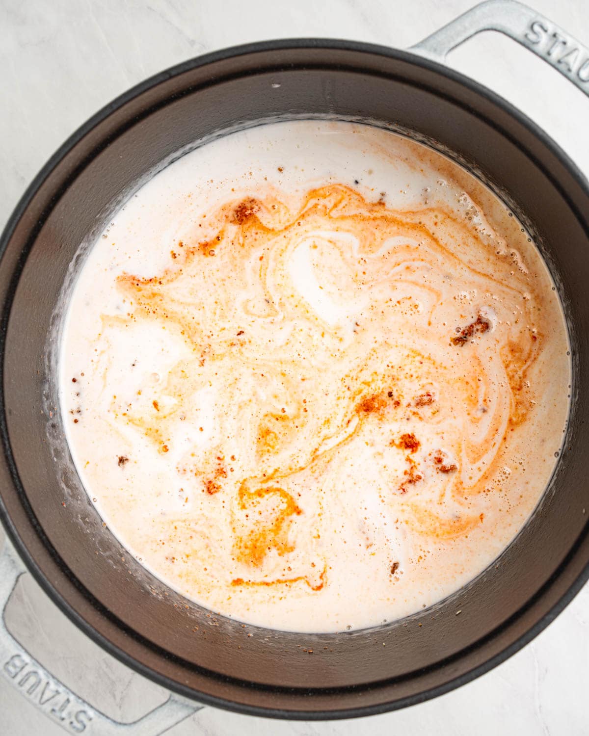 mixing together red curry paste and coconut milk in pot.