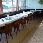 Eine lange Tafel mit weißen Tischdecken und Holzstühlen in einem Restaurant.