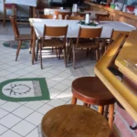 Holzbarhocker stehen in einem Restaurant mit Tischen und Stühlen im Hintergrund.