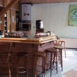 Holzbar mit Hockern und Kücheneinrichtungen im Hintergrund.