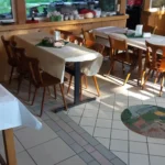 Ein Restaurant mit mehreren Tischen und Stühlen, die mit weißen Tischdecken bedeckt sind.