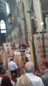 Farbenfrohe Prozession mit Fahnen der Sebastianus & Afra Schützenbruderschaft im Kölner Dom, festliche Stimmung, Gläubige in traditioneller Tracht, historische Schützenfahnen, religiöse Feierlichkeit, kirchliches Ereignis, traditionelles Brauchtum in Köln.