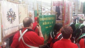 Farbenfrohe Parade mit Mitgliedern des Domstädter Köln e. V. bei Karneval, festliche Uniformen, Fahnen und Vereinswappen, traditionelles Brauchtum in Köln.