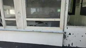 Beschädigtes Fenster mit zerbrochenem Glas und einem Sicherheitshinweis in einer alten Bushaltestelle in Köln.