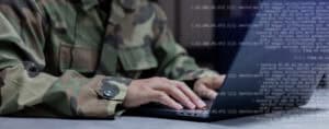 Person in military camouflage uniform typing on a laptop computer.