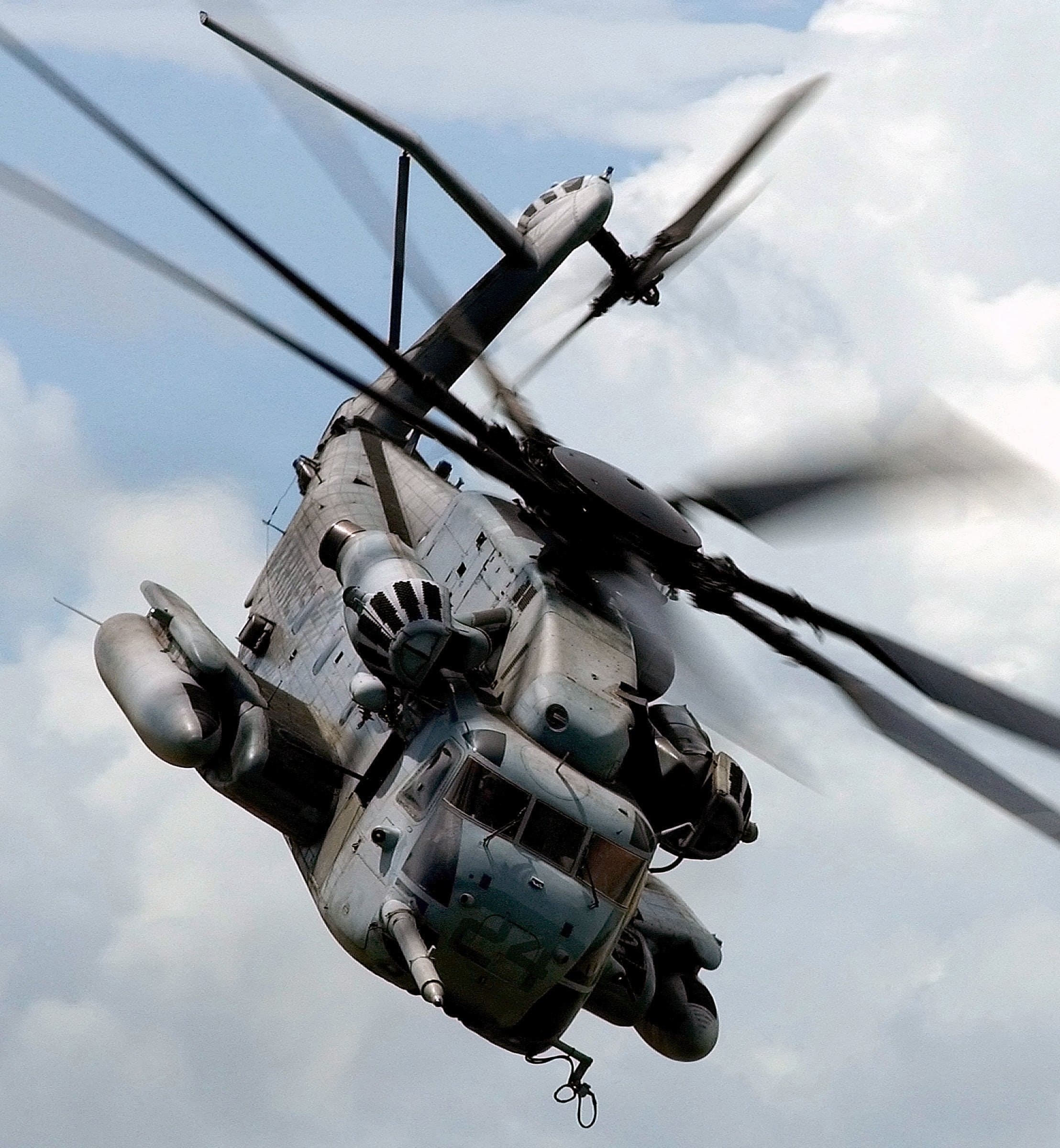 Large grey military helicopter flying against a cloudy sky