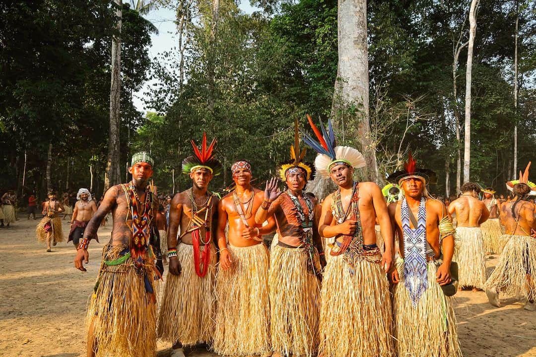 Traditional indigenous men celebrating in cultural attire with grass skirts and feathered headdresses at a vibrant outdoor event.