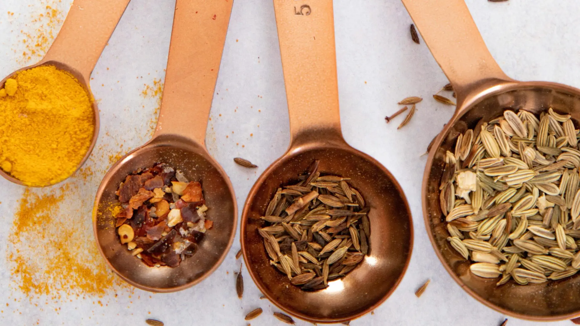 copper measuring spoons filled with turmeric, a spice mix, cumin seeds and fennel seeds