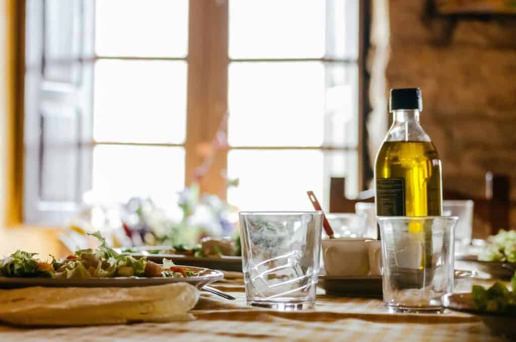 Bottle of olive oil on a dinner table with glasses and salad, representing healthy home-cooked meals with plant-based fats