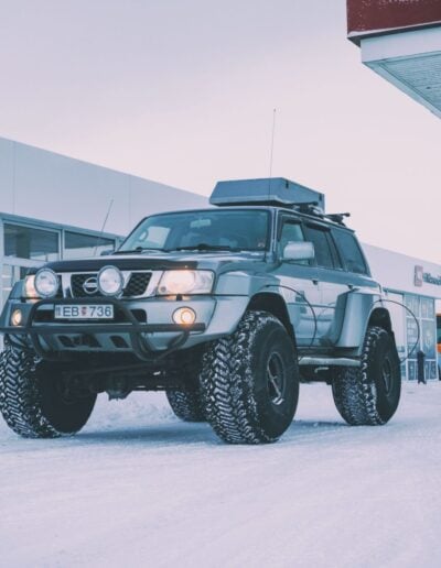 A large super jeep from Southcoast Adventure on very big wheels with a house, car, bus and people in the background.