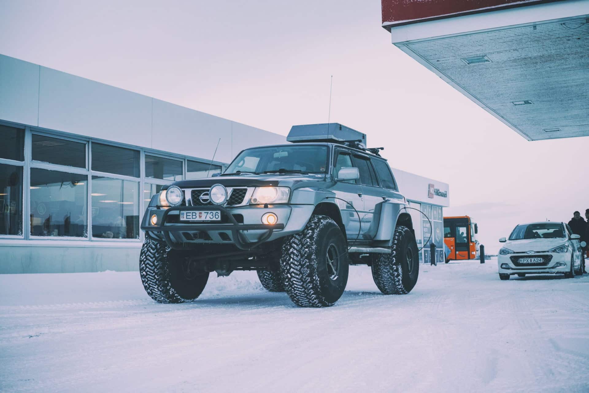A large super jeep from Southcoast Adventure on very big wheels with a house, car, bus and people in the background.
