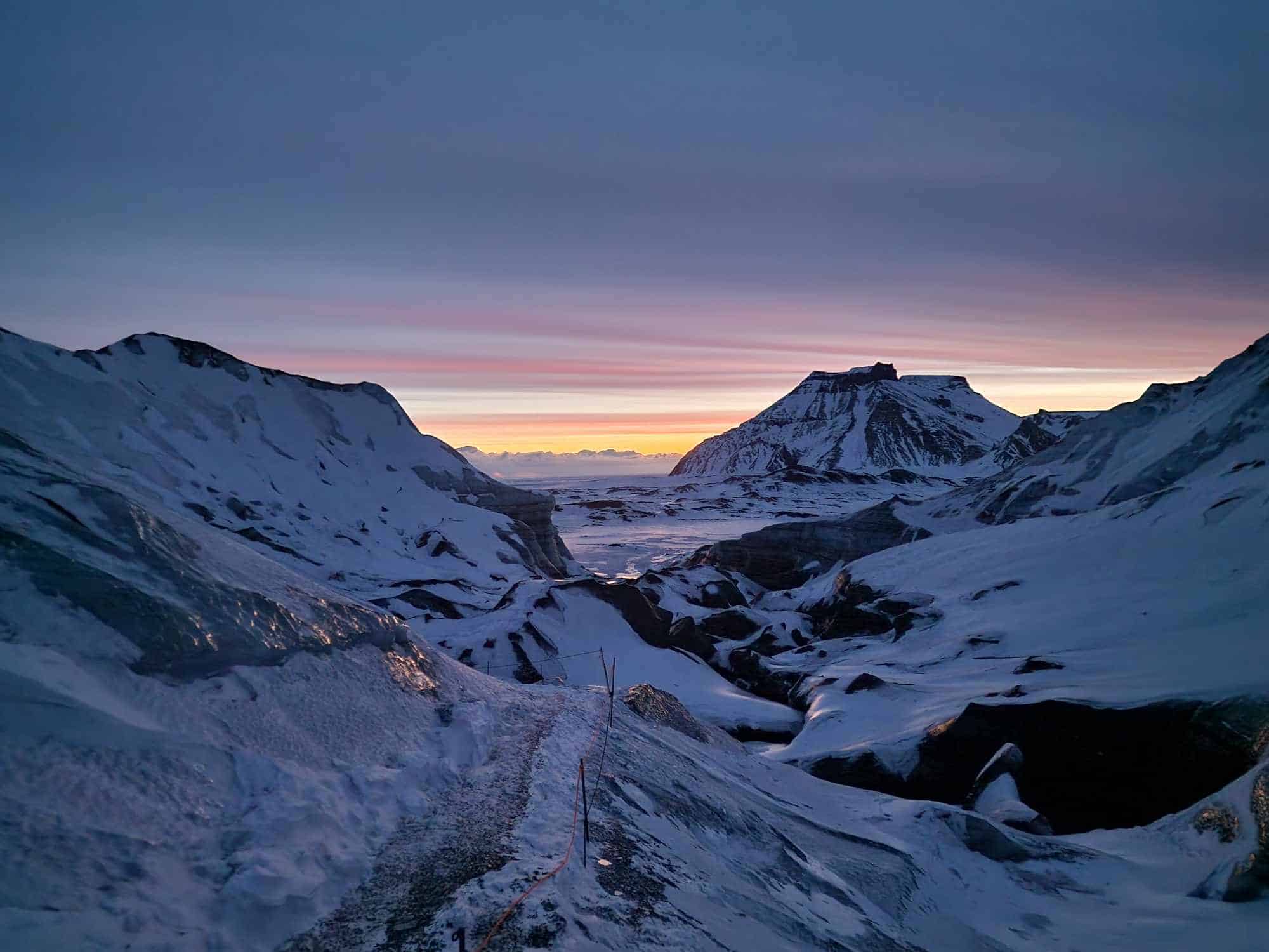 Snowy mountains and ice with orange and pink sky and Katla mountain.