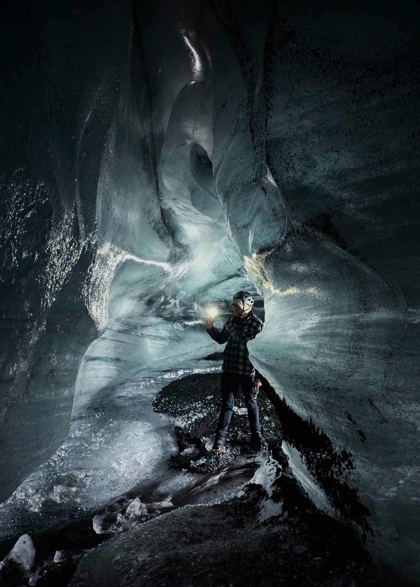 A person standing inside a Katla Ice Cave holding a flash light