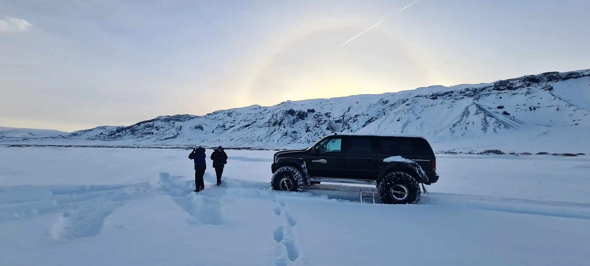 Snowy and icy mountains and deep snow on the ground with two persons on a super jeep tour with southcoast adventure.