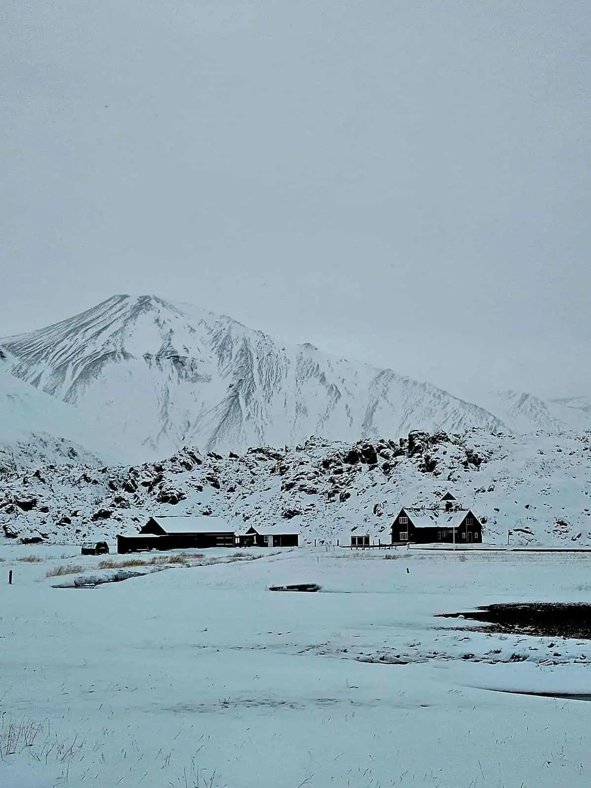 Snowy mountains and ground with three houses with white snowy roofs.