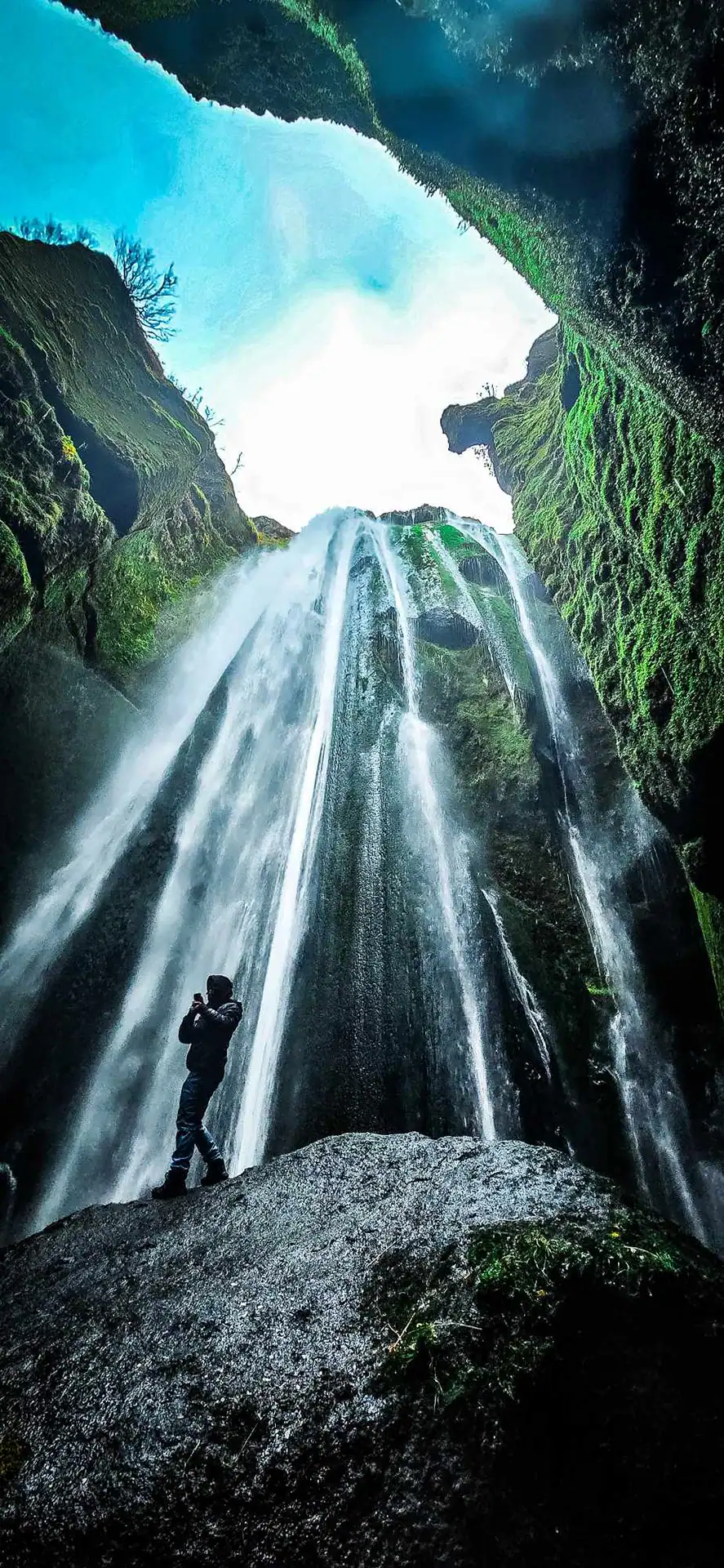 Waterfall with the view from the bottom up to the sky. A person standing on a large stone.