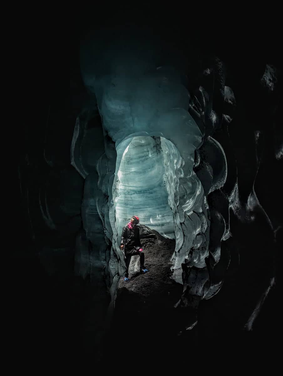 A person standing inside Katla Ice Cave. A view inside a dark tunnel of ice.