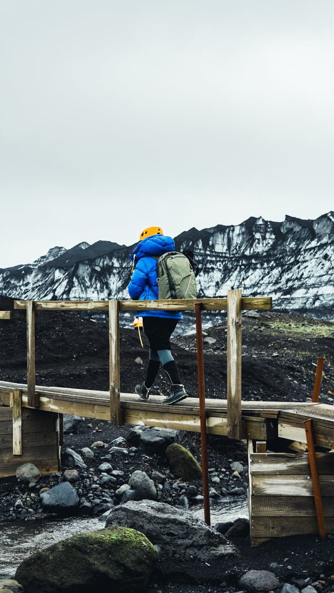 A person wearing a blue jacket walking on a small woody bridge on a Katla Ice Cave tour with Southcoast Adventure