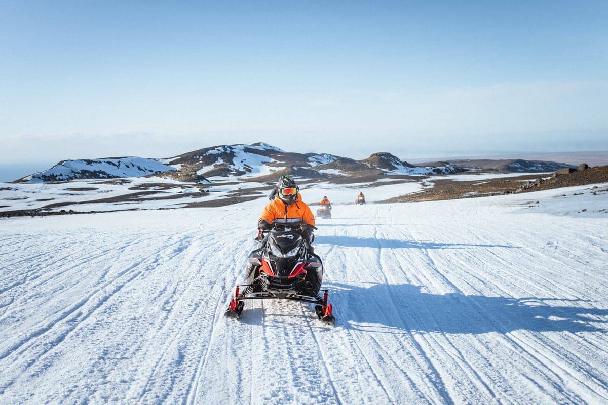 A person driving a snowmobile on Eyjafjallajokull ice with mountain and clear sky in the back with Southcoast Adventure.