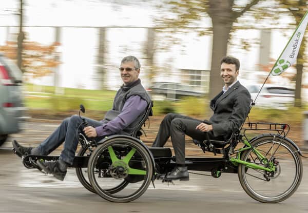 Dreirad-Tandem mit zwei Männern, Fahrrad mit elektrischem Antrieb, in Bewegung.