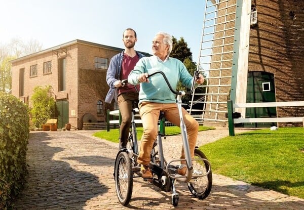 Senior und junger Mann fahren auf Dreirad-Tandem im Park.