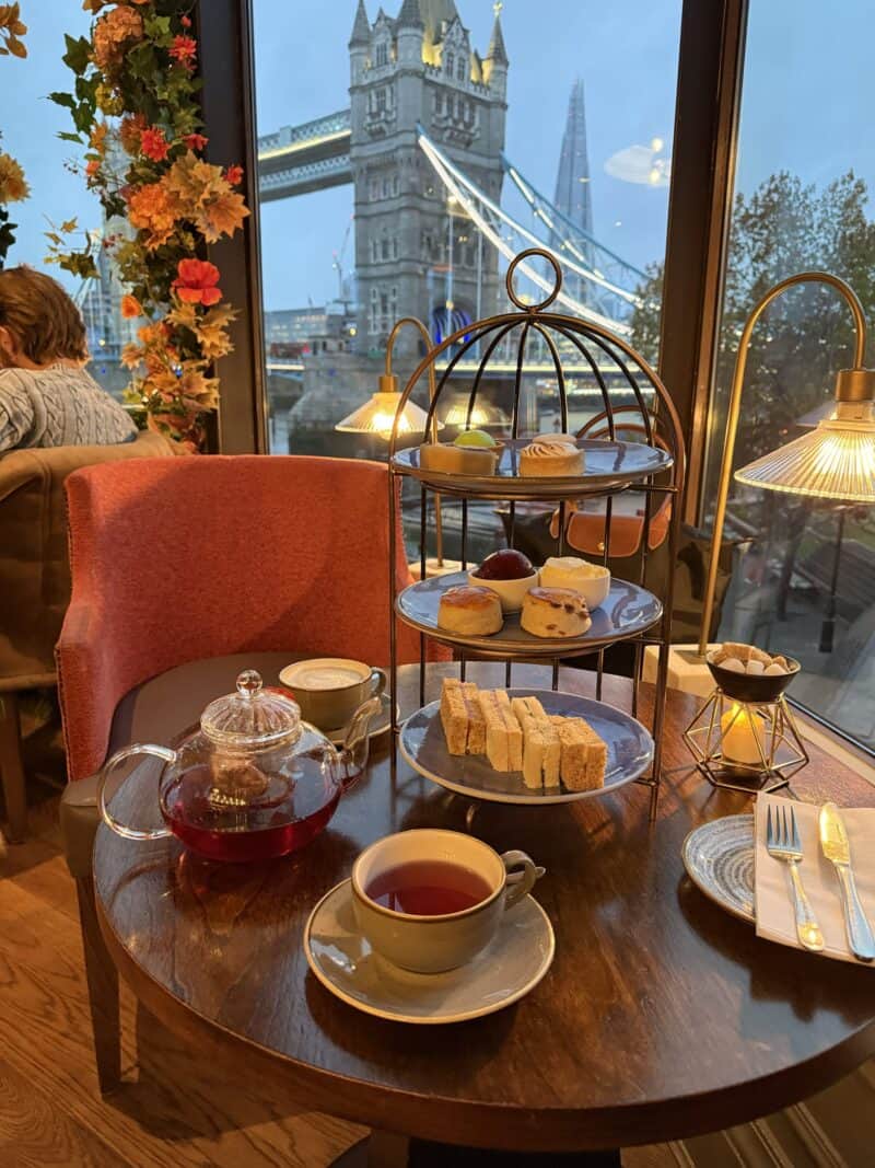 Indoor breakfast setup with tea, cake, and pastries overlooking Tower Bridge in London.