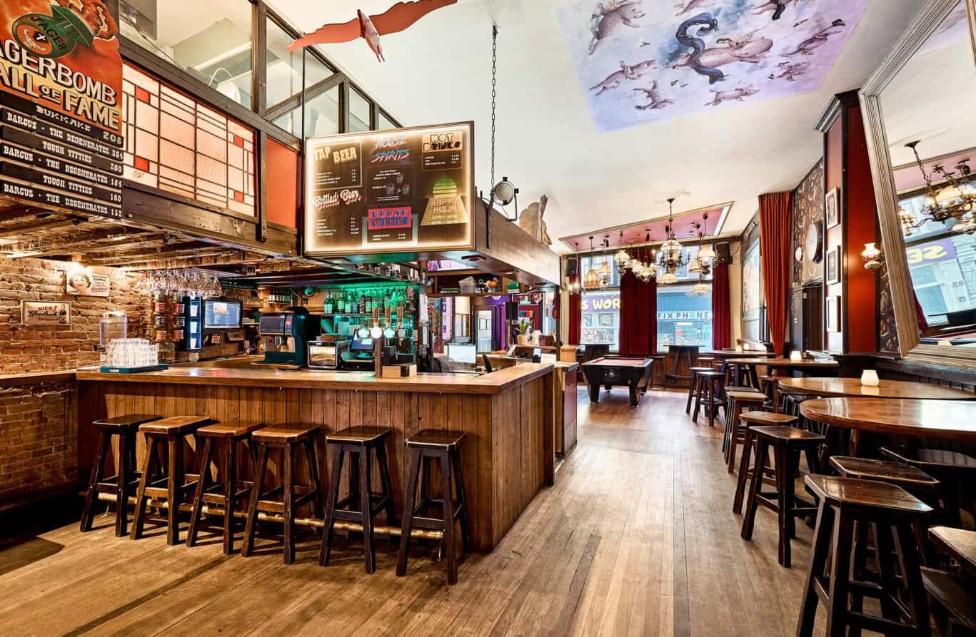 Bright bar area at Flying Pig Downtown hostel, featuring wooden stools, colourful lighting, and vibr.