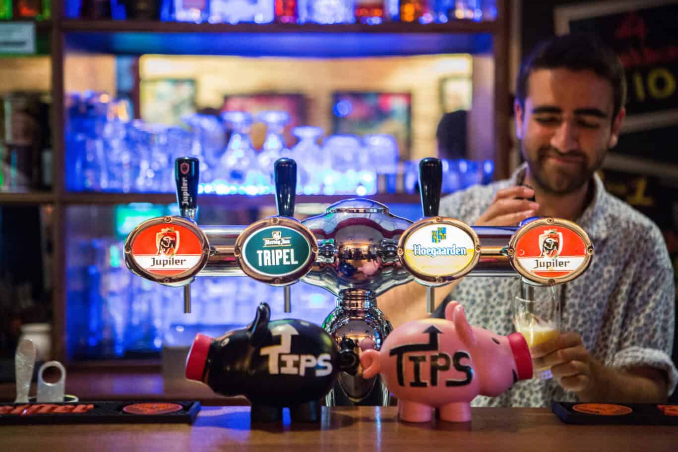 A bartender pours a beer at Flying Pig Uptown, a lively hostel bar with craft beer taps and a friend.