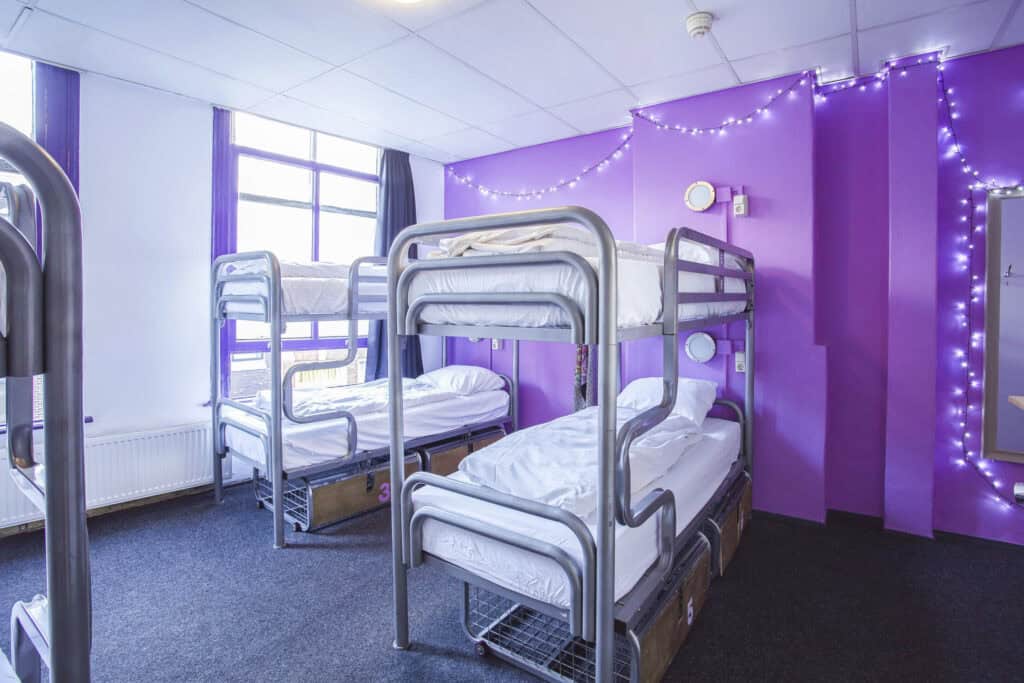 Bright dormitory room with metal bunk beds and colourful purple walls at Flying Pig Downtown Hostel.