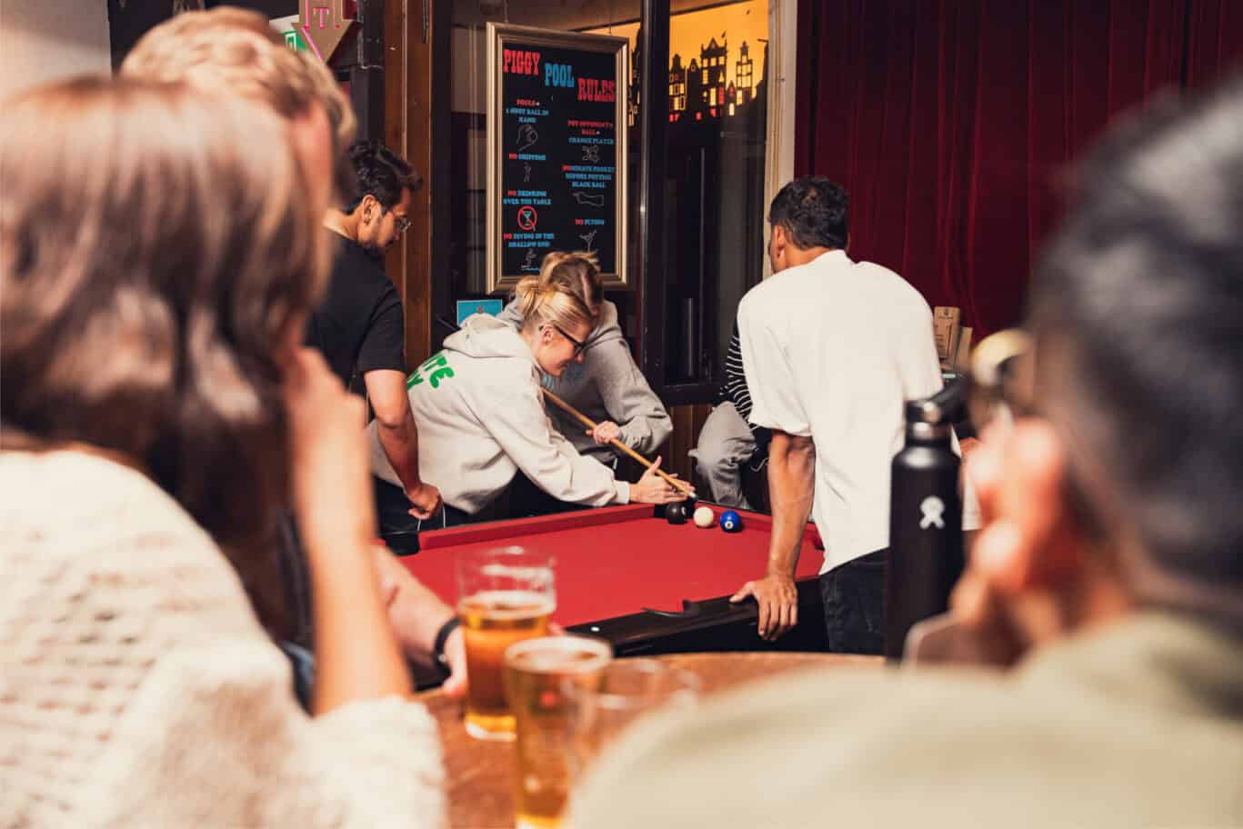 Pool table at Flying Pig Downtown hostel bar with guests enjoying a game.