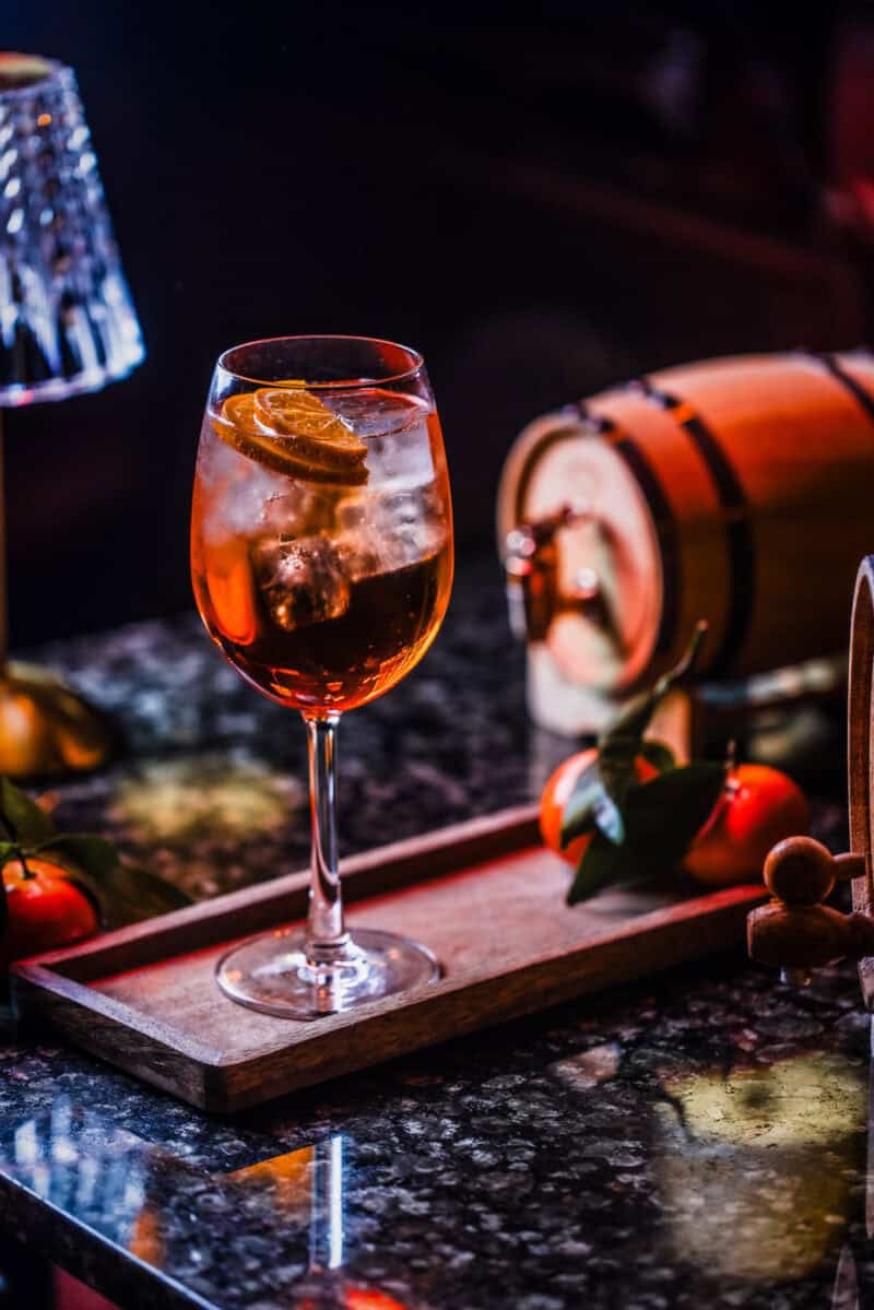 A refreshing cocktail served in a tall glass with ice and a slice of citrus fruit, set on a dark mar.