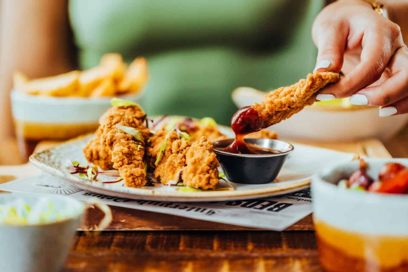 Delicious fried chicken being dipped in sauce at a restaurant.