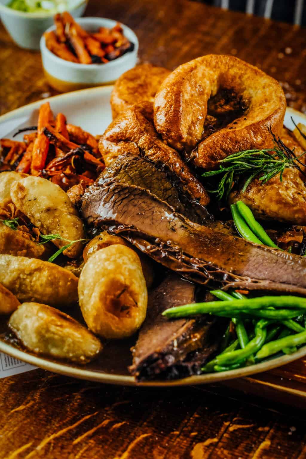 A hearty British Sunday roast featuring beef, Yorkshire pudding, roast potatoes, green beans, and ca.