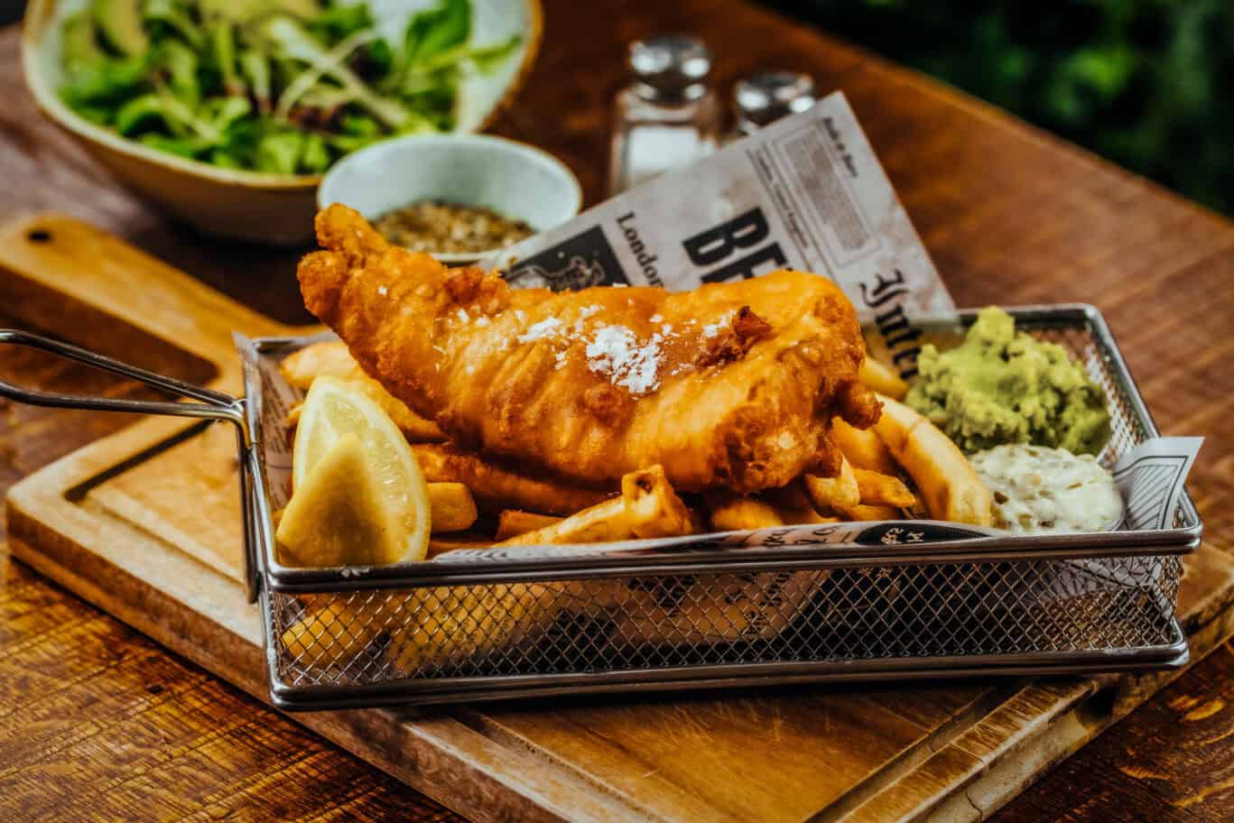 Classic fish and chips served with lemon, peas, and tartar sauce on a wooden table.