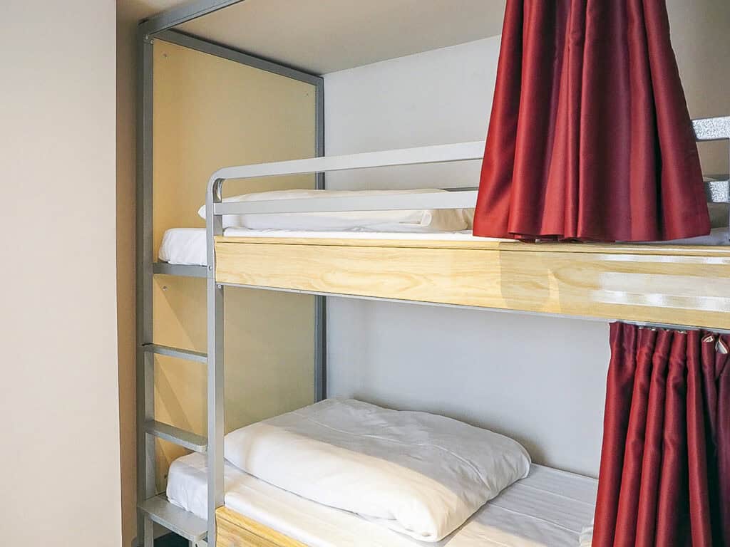 Bunk bed with white bedding and red curtains at St Christopher’s Liverpool Street hostel.
