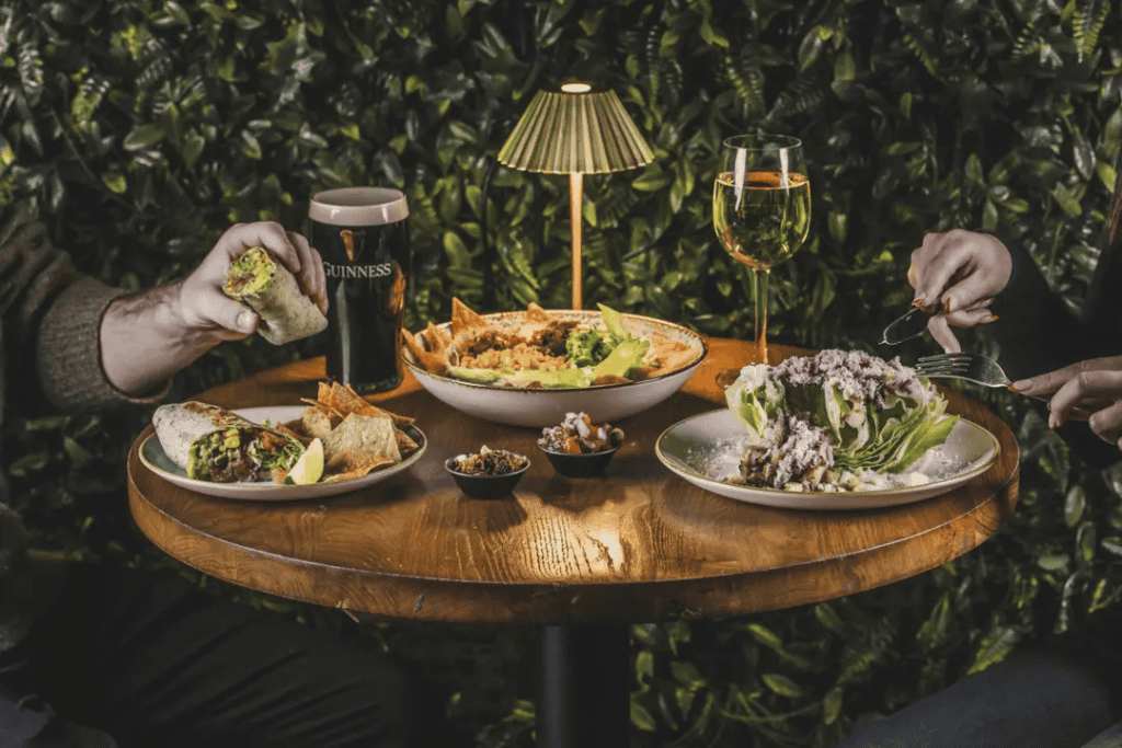 Casual dining with drinks and food at London Bridge Hostel, vibrant greenery background.