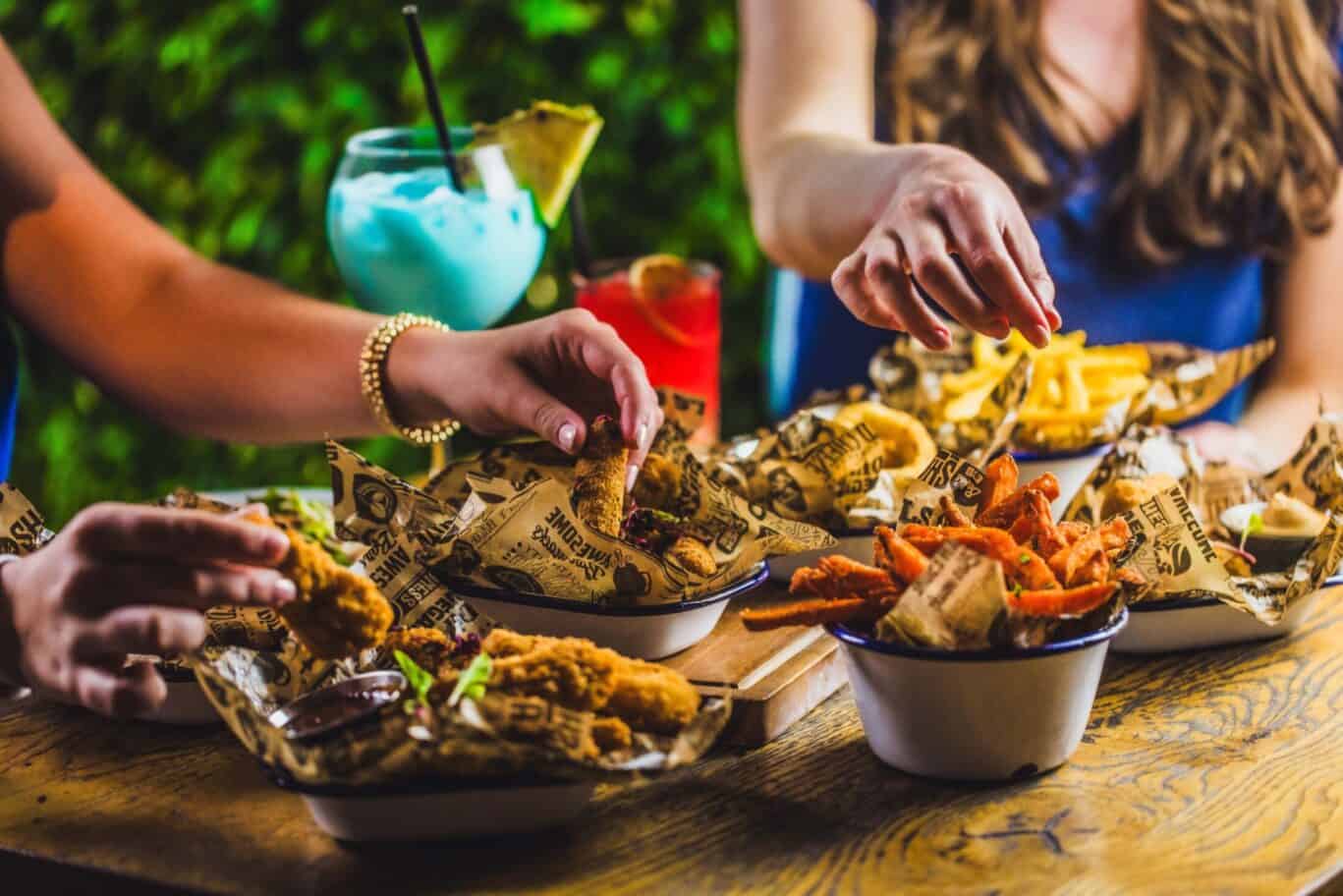 People enjoying a variety of fried foods and colourful drinks at a casual outdoor dining table.