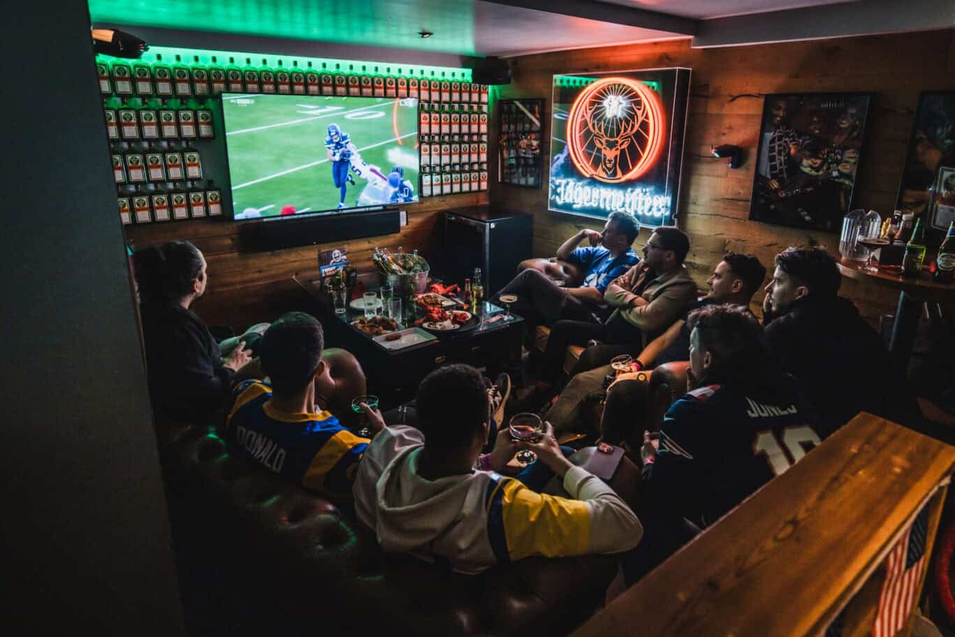 Group of friends watching a football match on a large screen at a lively sports bar.