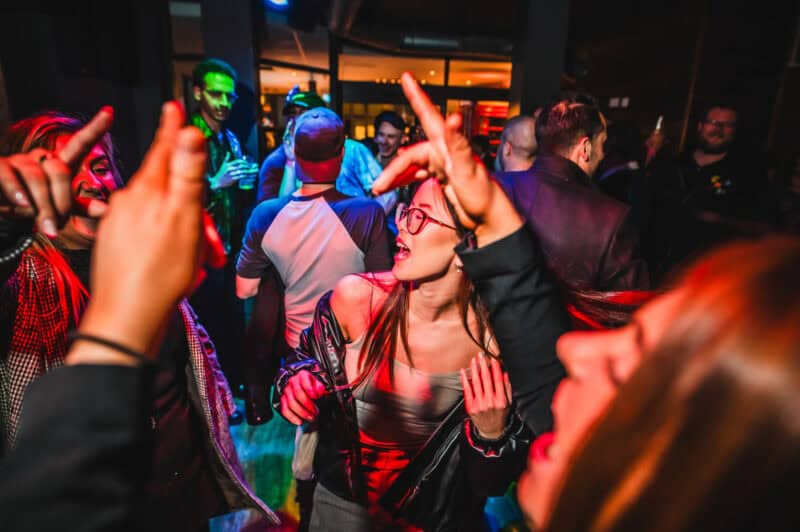 Lively group of young people dancing and socialising at night in a vibrant hostel bar.