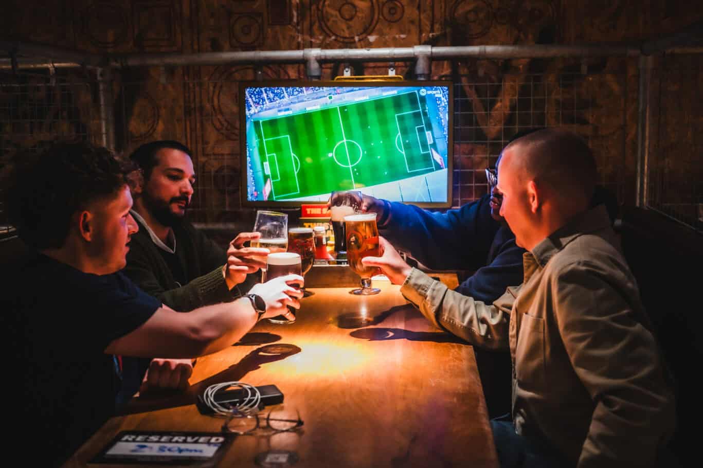Group of friends enjoying drinks while watching a football match on a TV at London Bridge Hostel.