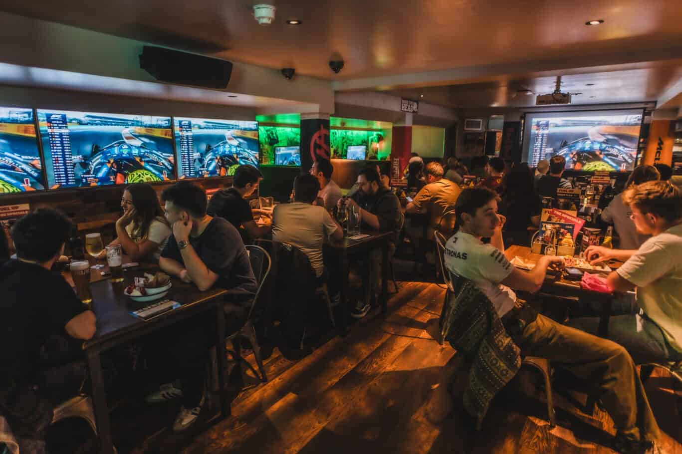 Busy gaming lounge at London Bridge hostel with guests playing video games on large screens.