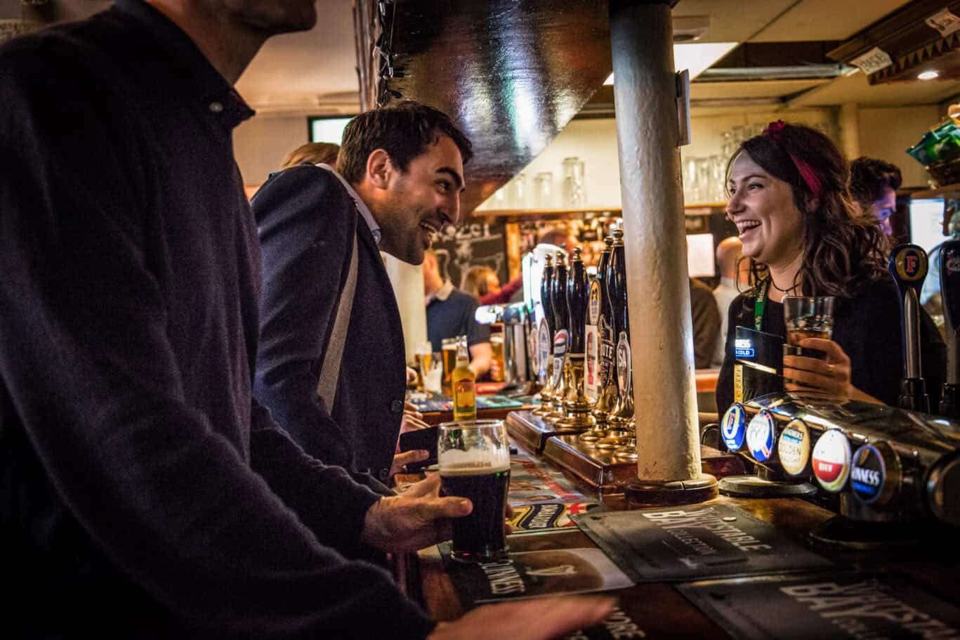 Bar scene at Liverpool Street Hostel with smiling guests and drinks on tap.