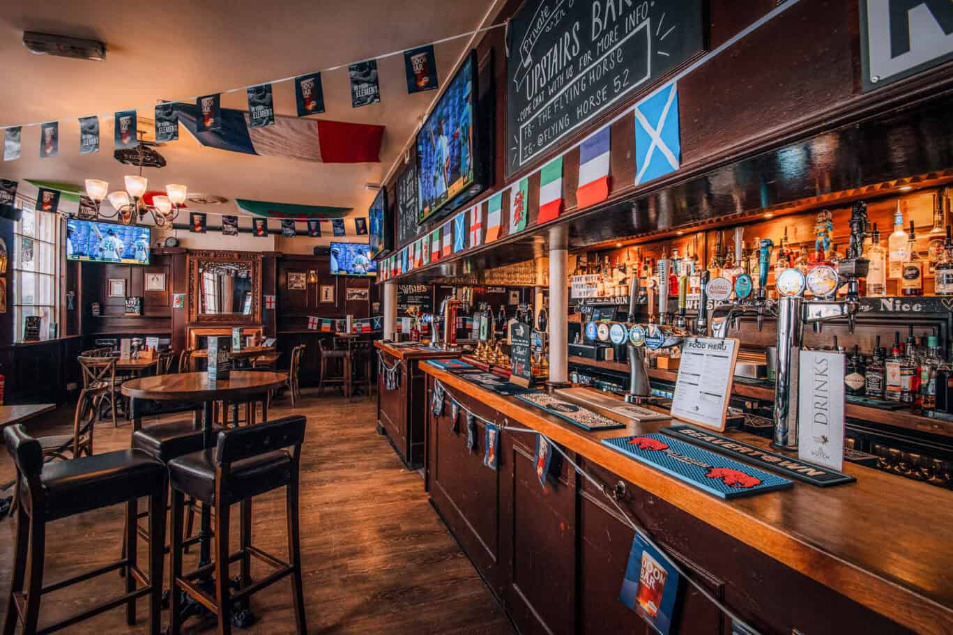 Interior view of Liverpool Street Hostel bar with flags and TV screens.