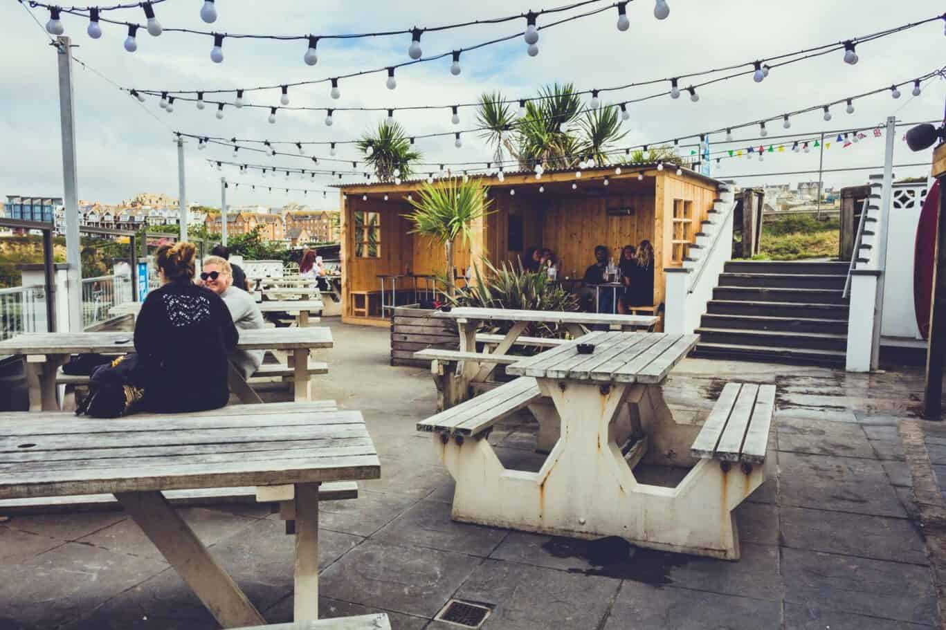 Outdoor seating area at St Christopher’s Newquay hostel with picnic tables and string lights.