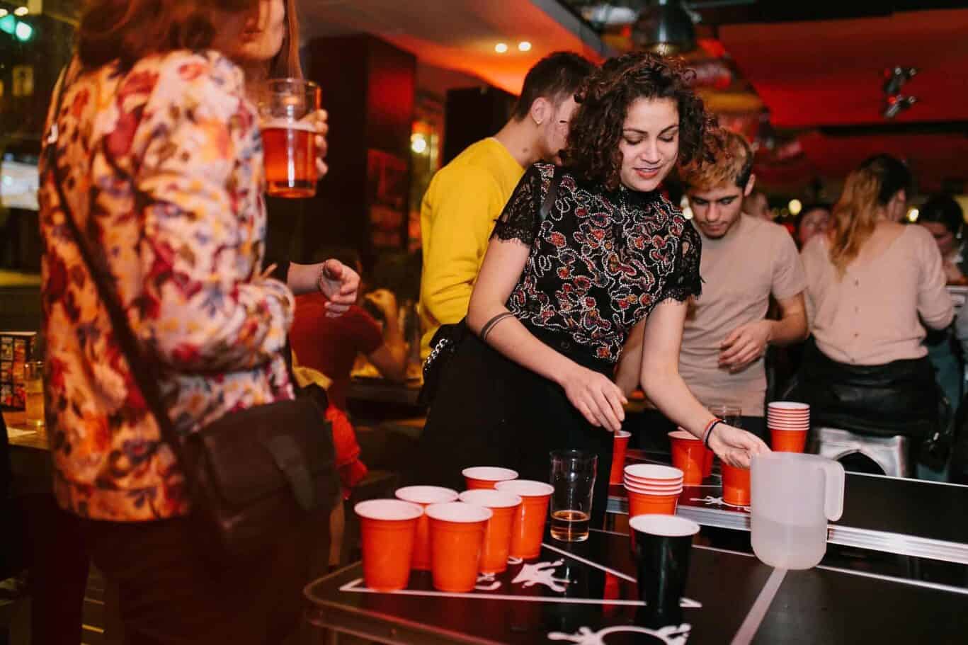 Group of young adults enjoying beer pong game at St Christopher’s Newquay hostel bar.