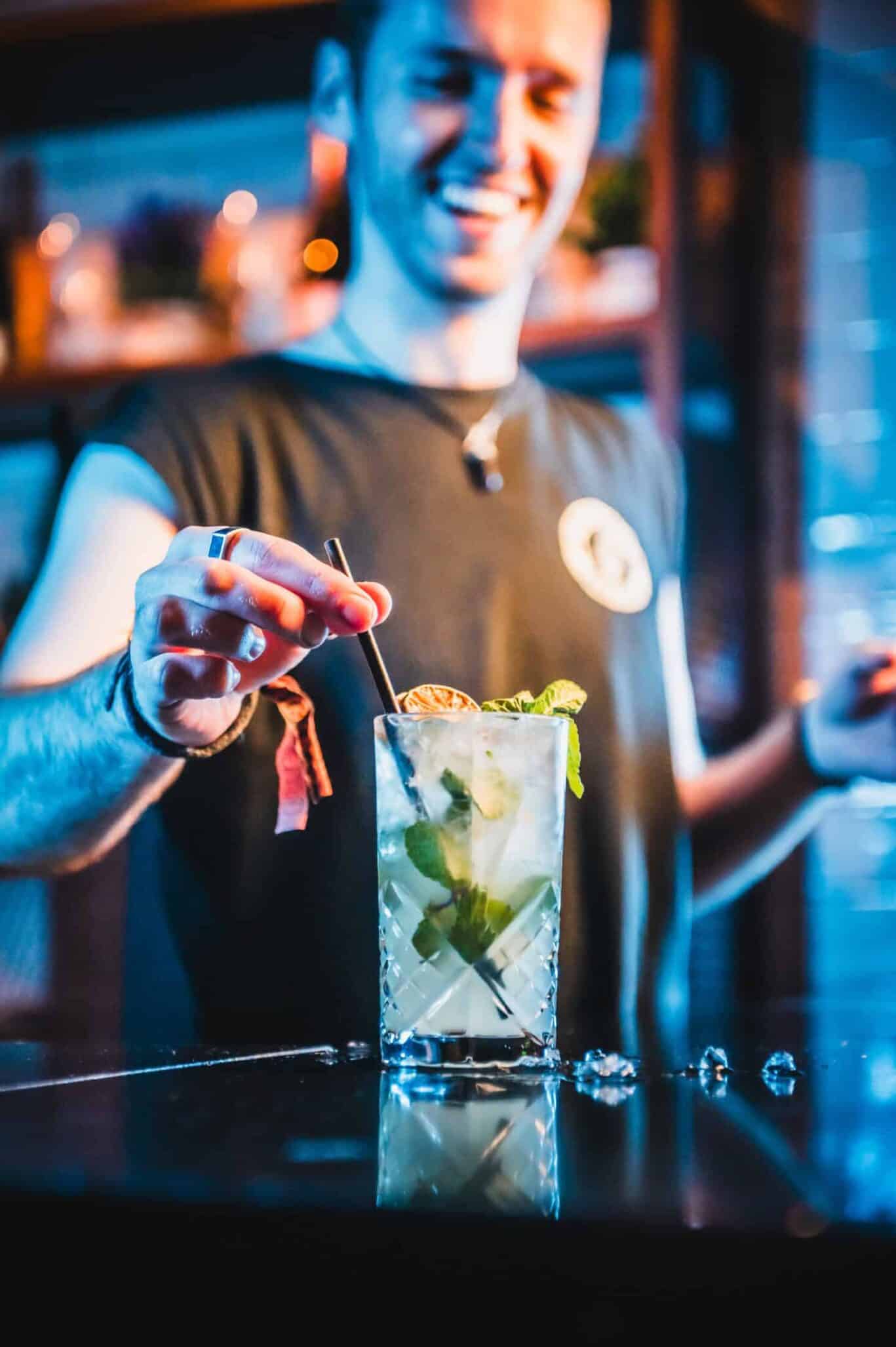 Young bartender preparing a refreshing mojito cocktail at St Christopher’s Newquay hostel bar.