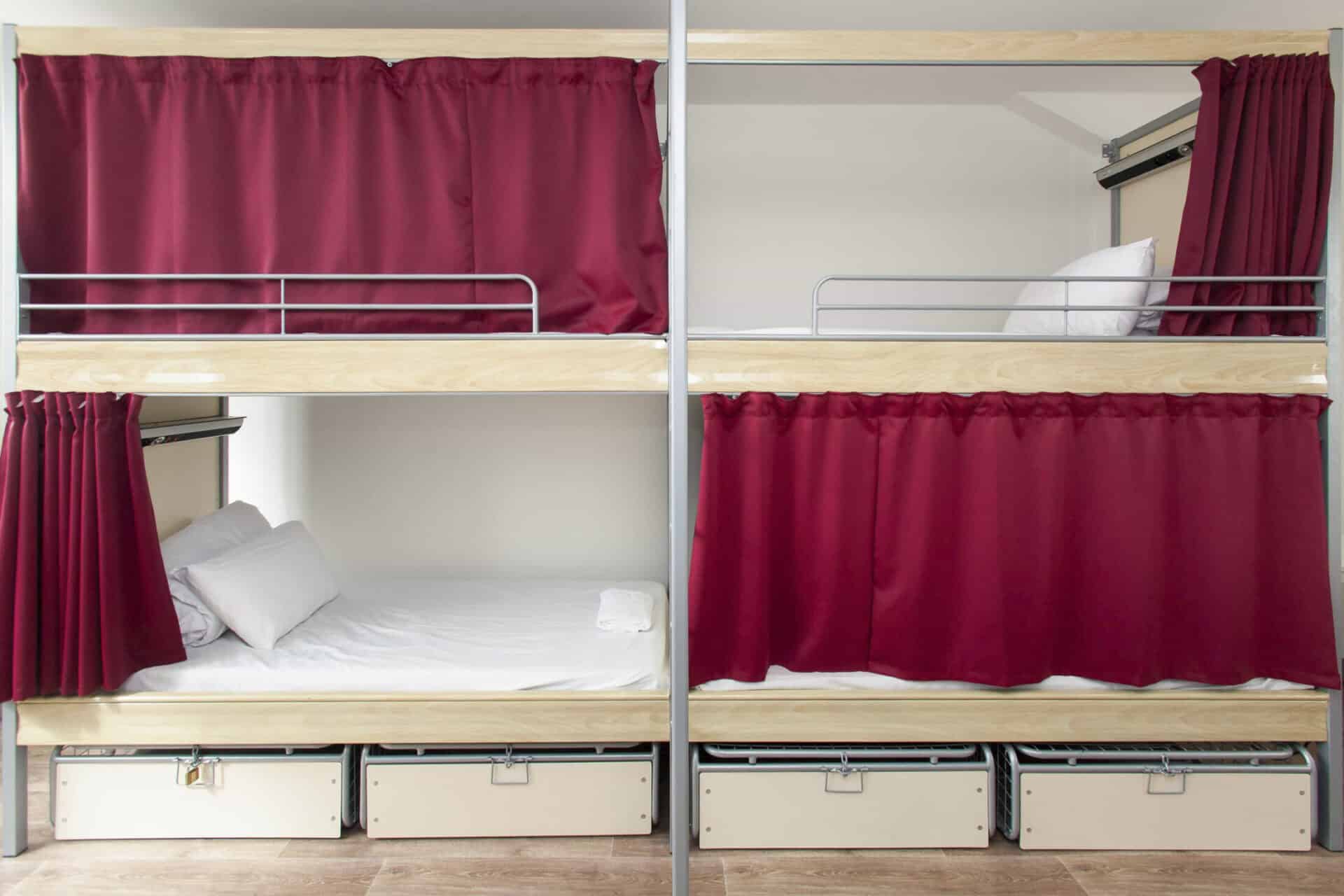 Bunk beds with red curtains and white bedding at St Christopher’s Paris - Gare du Nord.