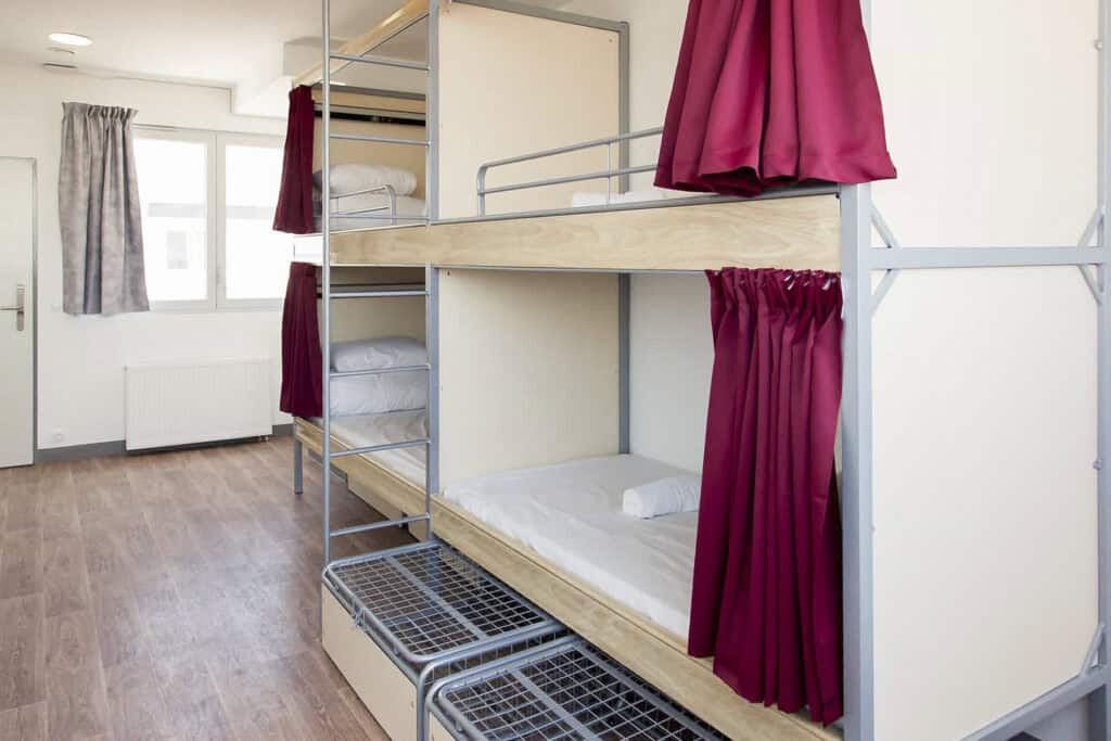 Bunk beds with privacy curtains in a bright, modern dormitory room.