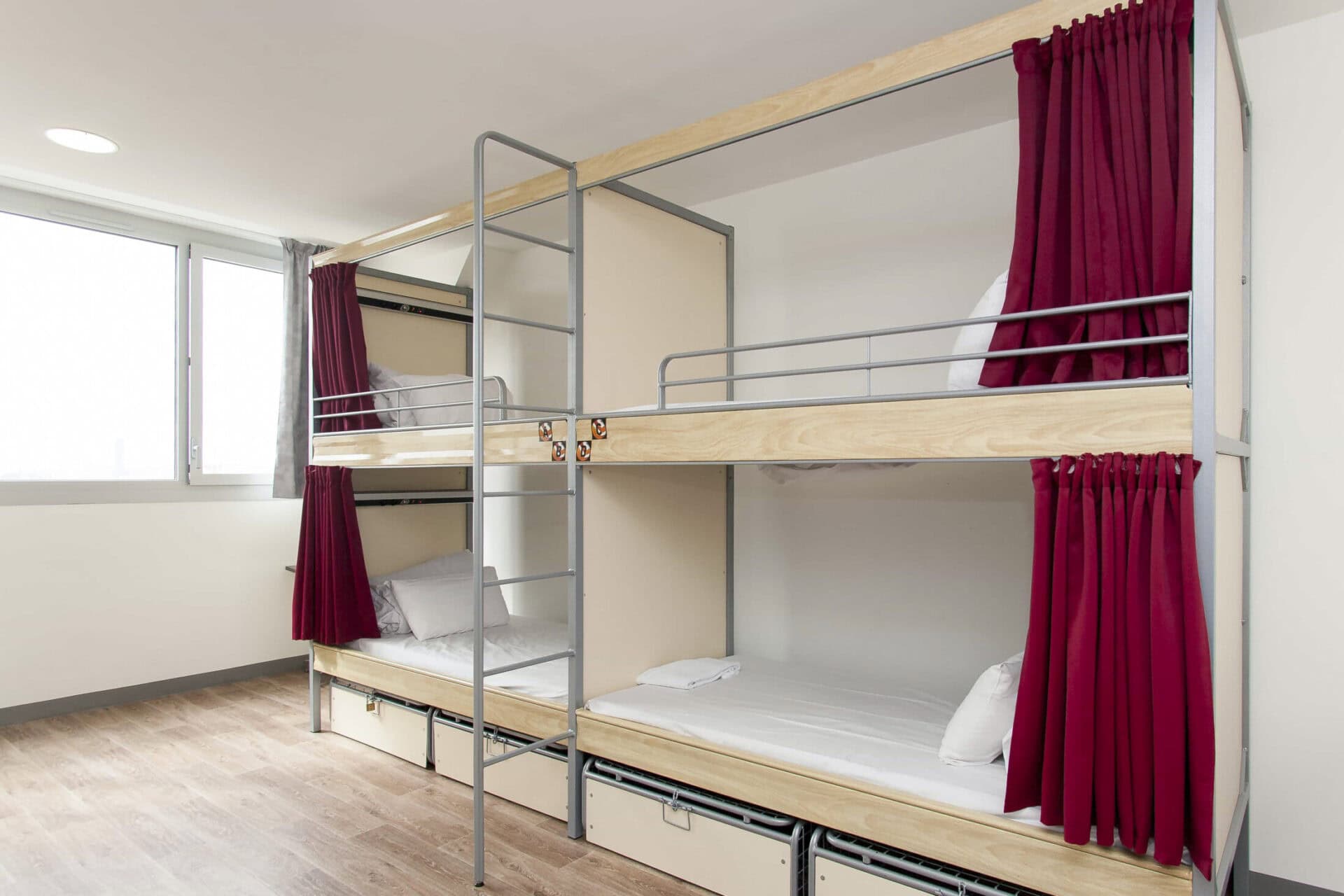 Hostel dormitory with bunk beds and red curtains at Gare du Nord, Paris.